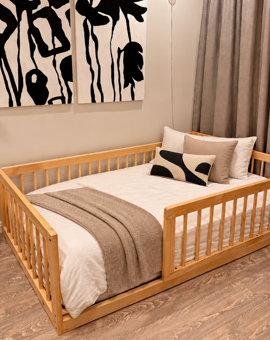 A light natural wood daybed with a slatted guard rail, styled with white bedding, a beige throw blanket, and decorative pillows in a modern bedroom setting.
