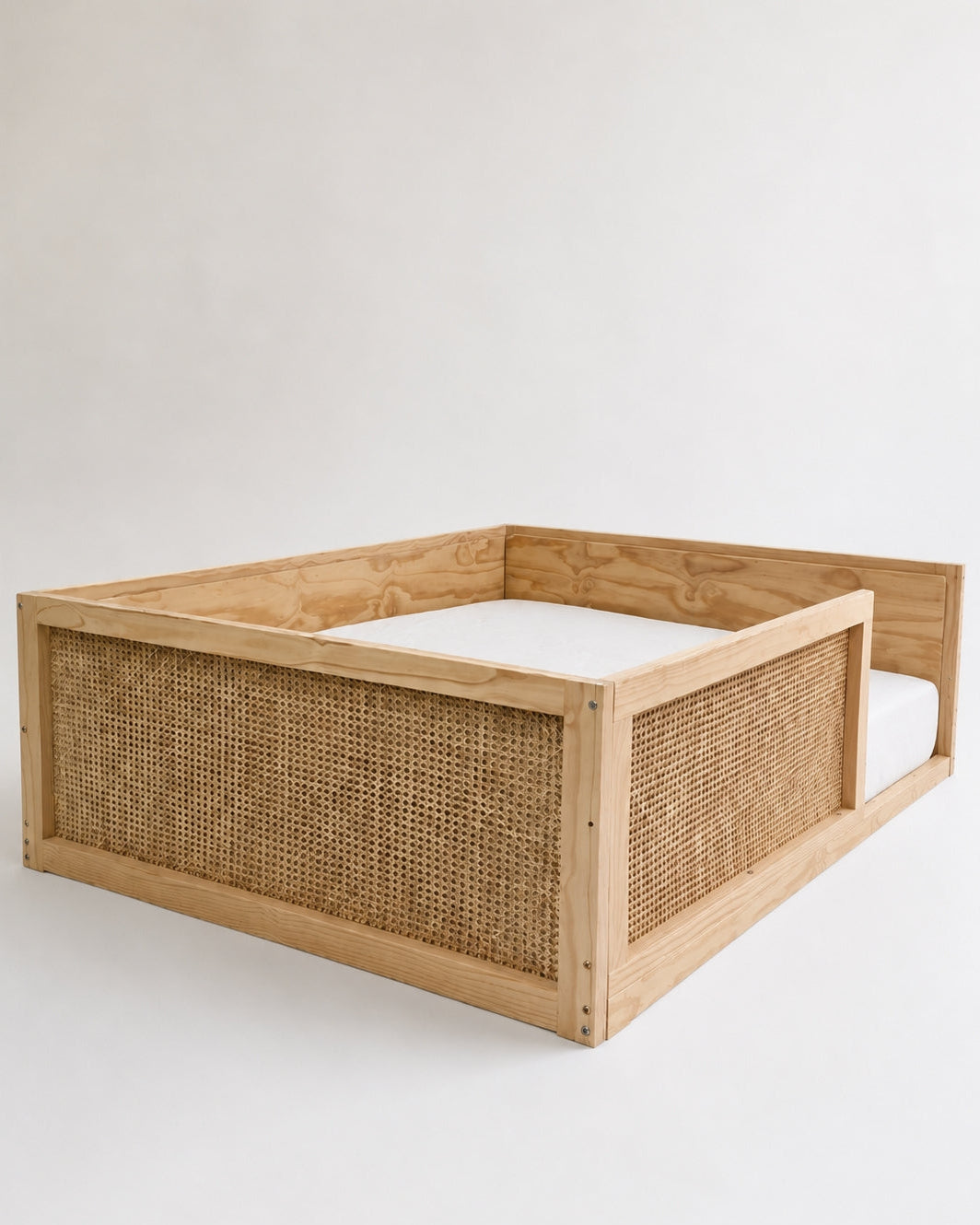 A wooden bed frame with woven cane panels on the sides, shown empty with a white mattress or bedding insert visible inside, photographed against a plain light background.